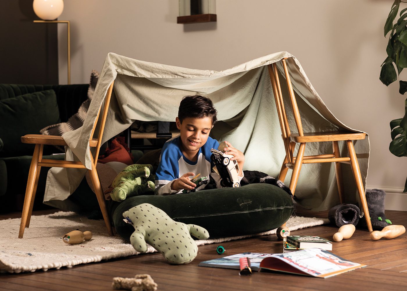A little boy is playing under a blanket fort.