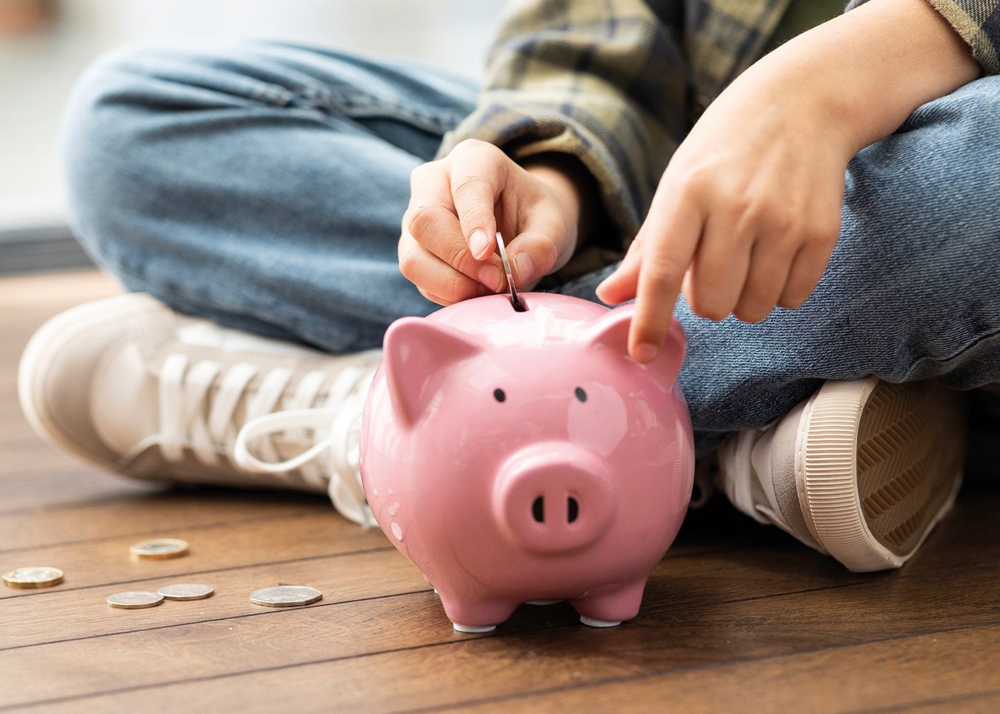 A person is dropping money into a little pink piggy bank.