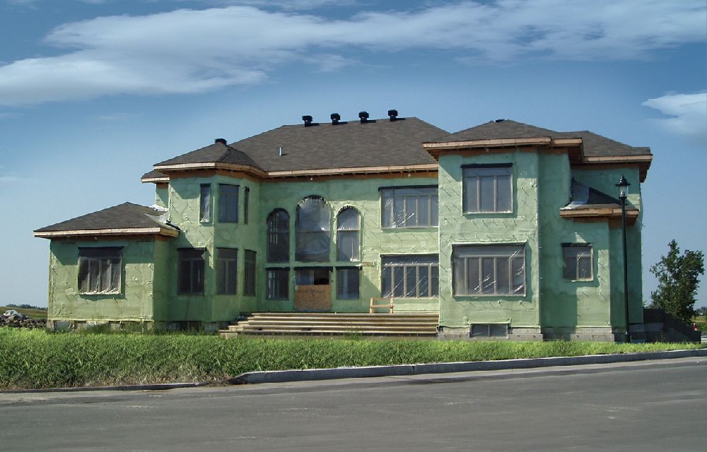 Large home under construction covered in green spray foam.